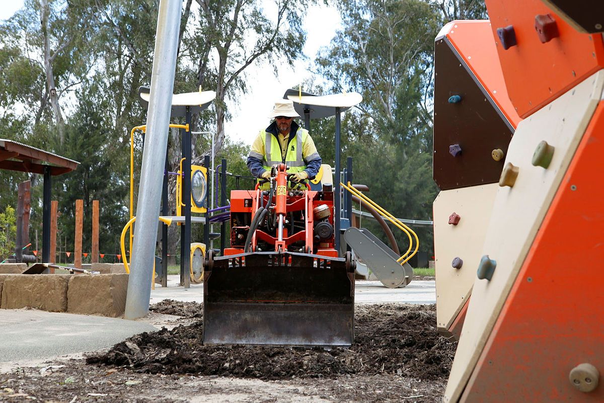 A man on a small piece of machinery cleans away mud from a children's playground after flooding. 