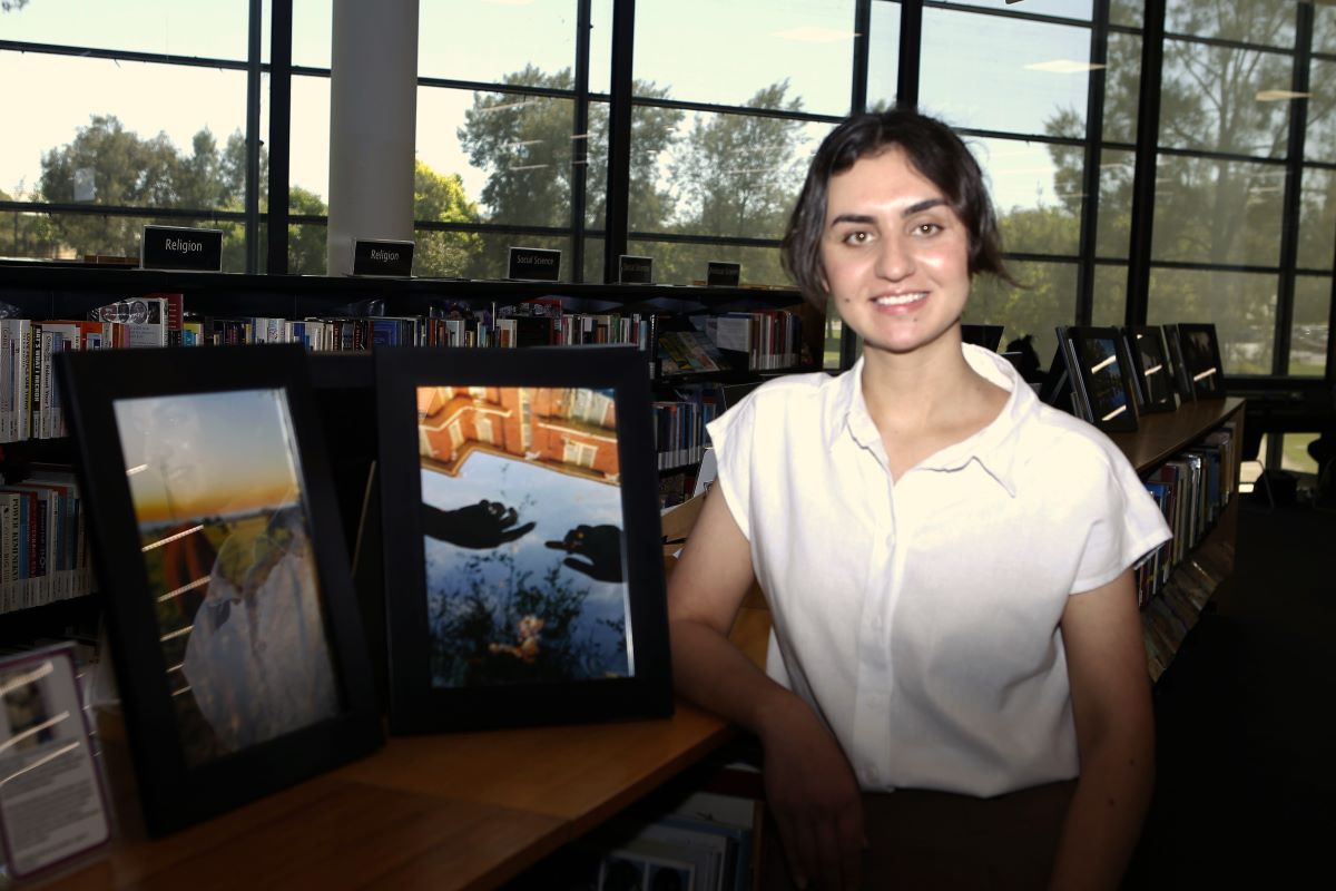 A young Iraqi-born woman standing in a public library with some photographs she took. 