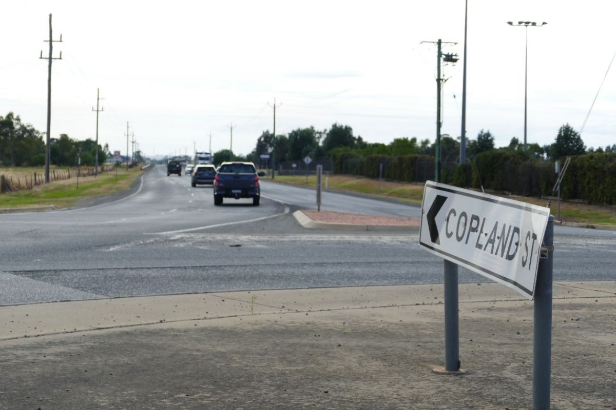 Street sign for Copland Street on roundabout in foreground, with traffic on road in background