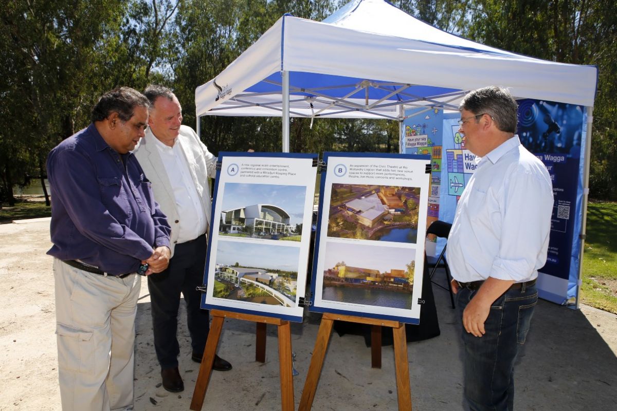 Three men standing next to marquee and A1 posters featuring  artist impressions of two projects proposed for Wagga Wagga.