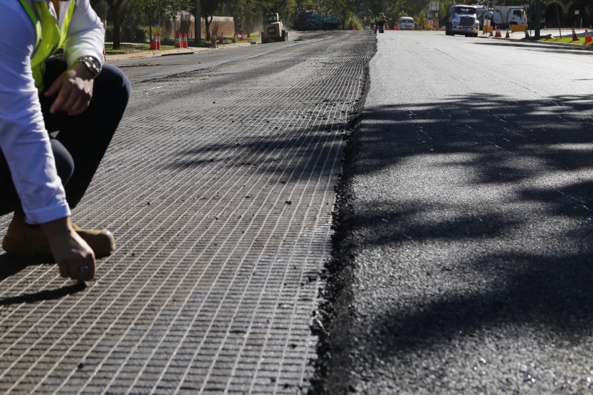 Man crouched down looking at Geogrid rolled out on road being rehabilitated. 