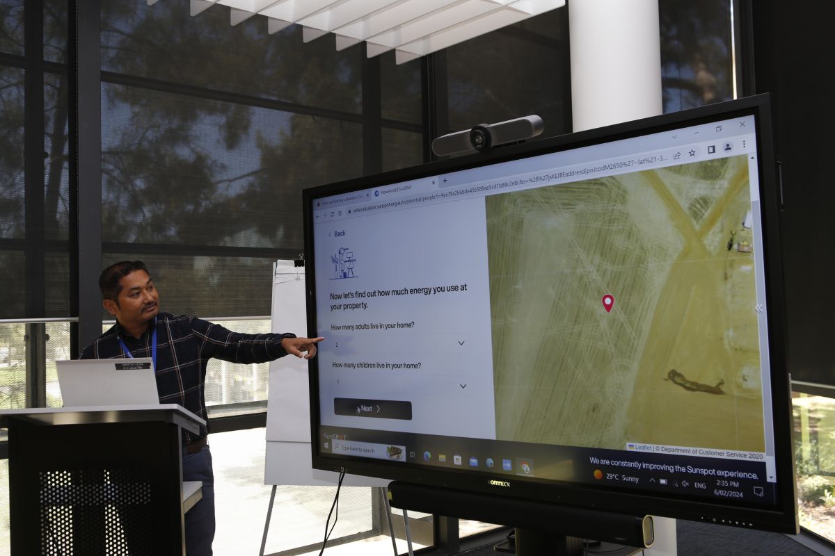Net Zero Emissions Project Officer Hemendra Chaudhary pointing towards a large screen showing a SunSPOT presentation.