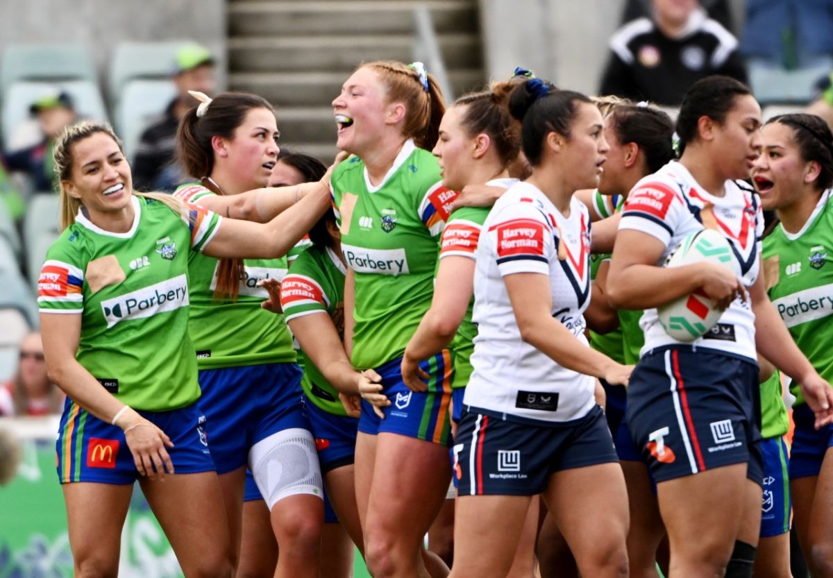 Women rugby league players in green Canberra Raiders celebrating on field