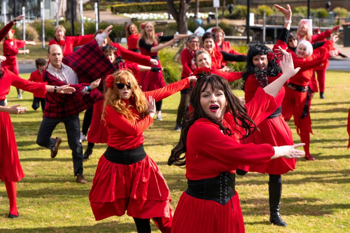 Group of females and males of mixed age, wearing red clothing and dancing.