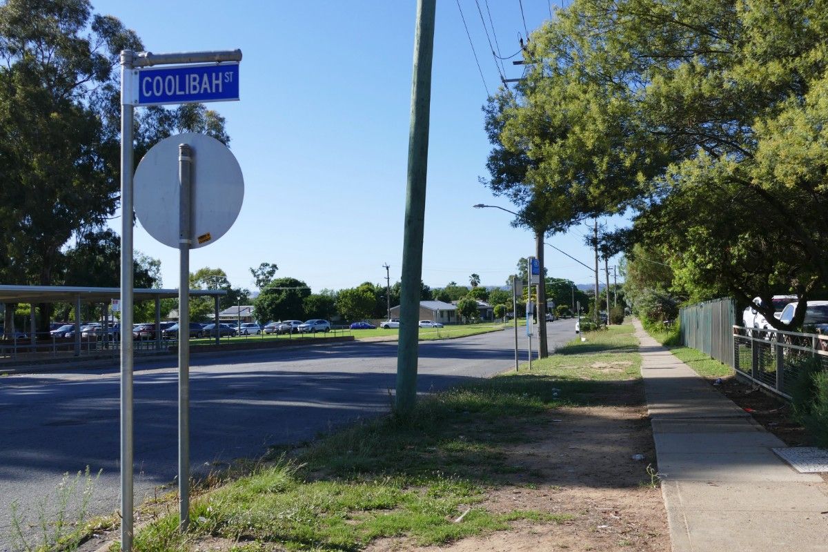 Suburban street with road sign for Coolibah Street on top right of image and footpath to left of street.