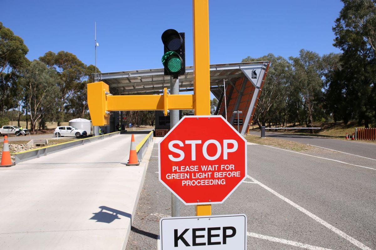 Stop sign stating please wait for green light before proceeding, with a waste management centre weighbridge in the background.