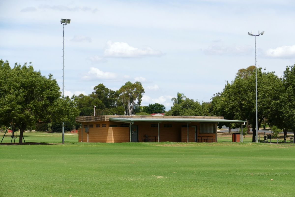 Front view of brick amenities building on a sporting oval, with light towers on either side of the building.