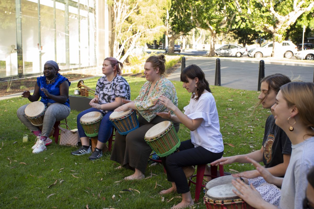 women and men sitting down playing African drums on grassy area