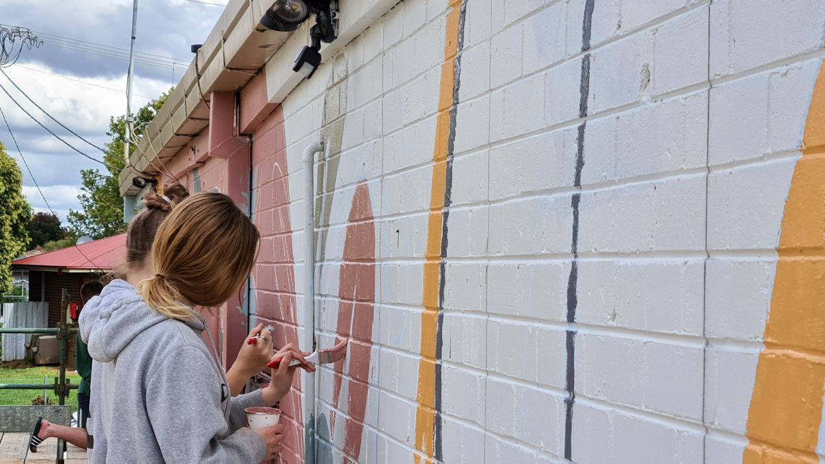 Two young women painting mural on brick wall