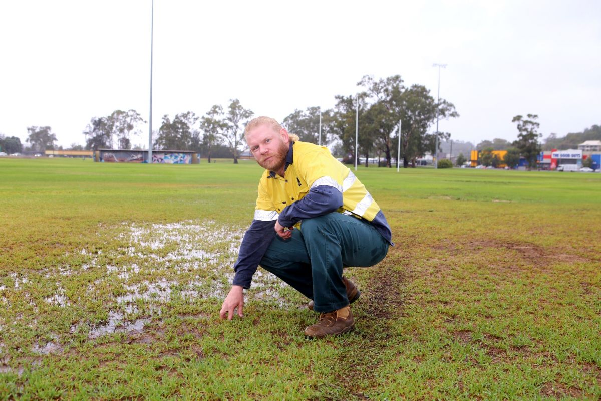 Man in high visibility jumper crouches down to test the wet ground at a sporting field
