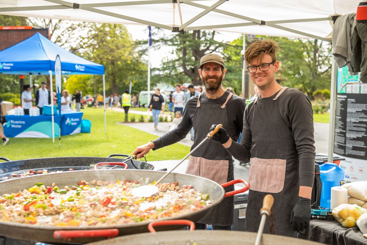 Two men preparing paella at a stall in the Victory Memorial Gardens