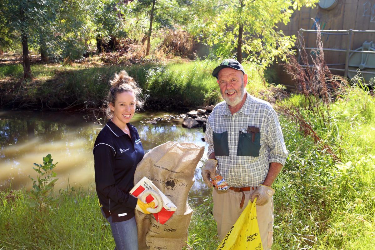 woman and man standing by lagoon, collecting rubbish and putting in bag