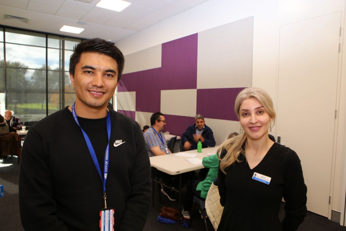 Man and woman standing at front of room with people at tables in background