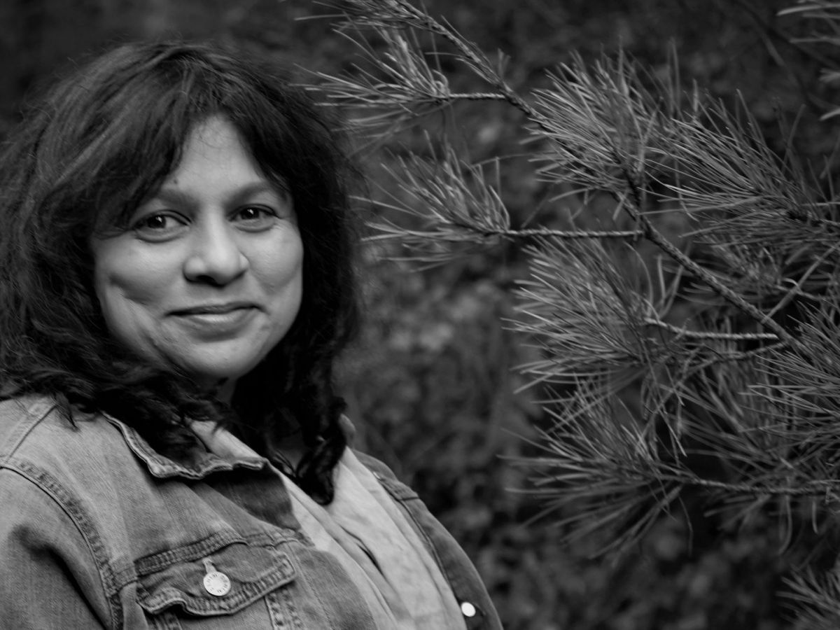 A black and white photo of a woman standing beside a fir tree