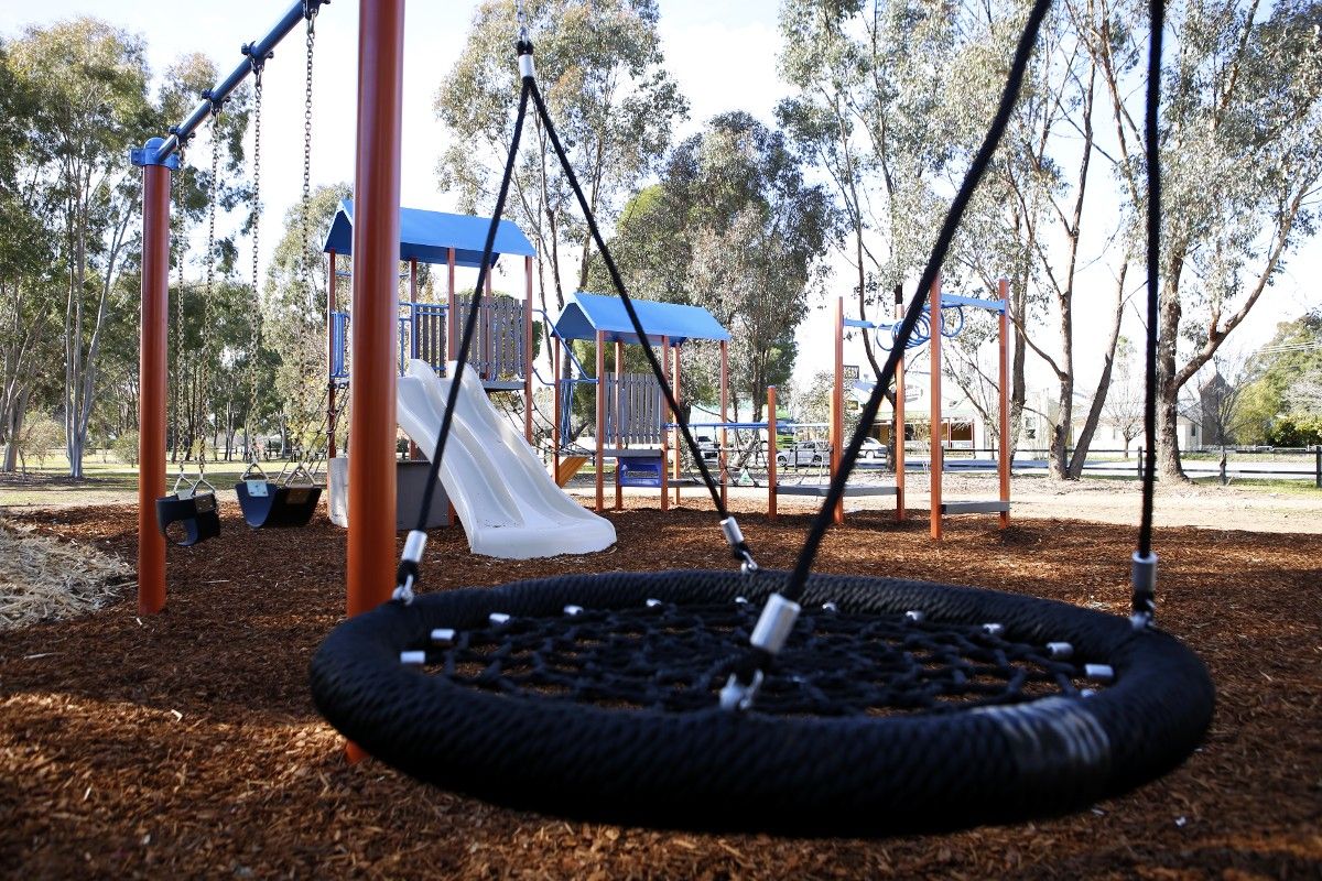 Round swing in foreground with other playground equipment in background