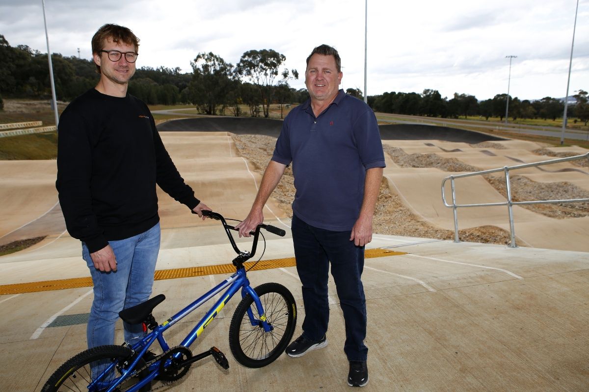 Two man standing beside bike on start ramp at BMX track