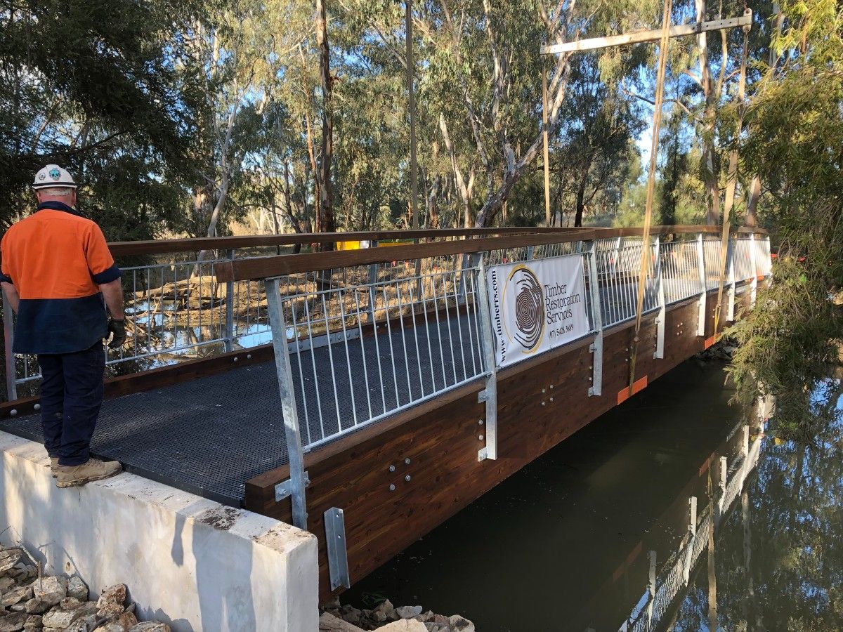 Man in hi-vis shirt standing on abutment at end of new footbridge