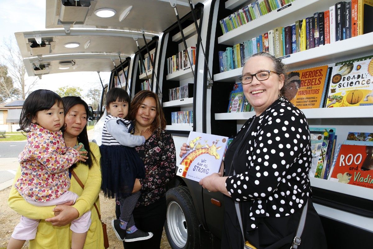 Two women with young female children and a third woman holding a book stand beside the new Agile Library van