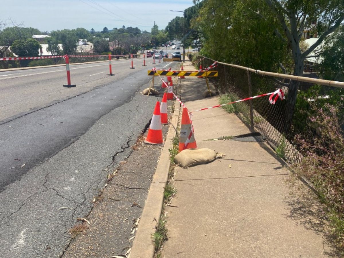 A section of slightly sunken footpath has been marked off by traffic cones and tape 