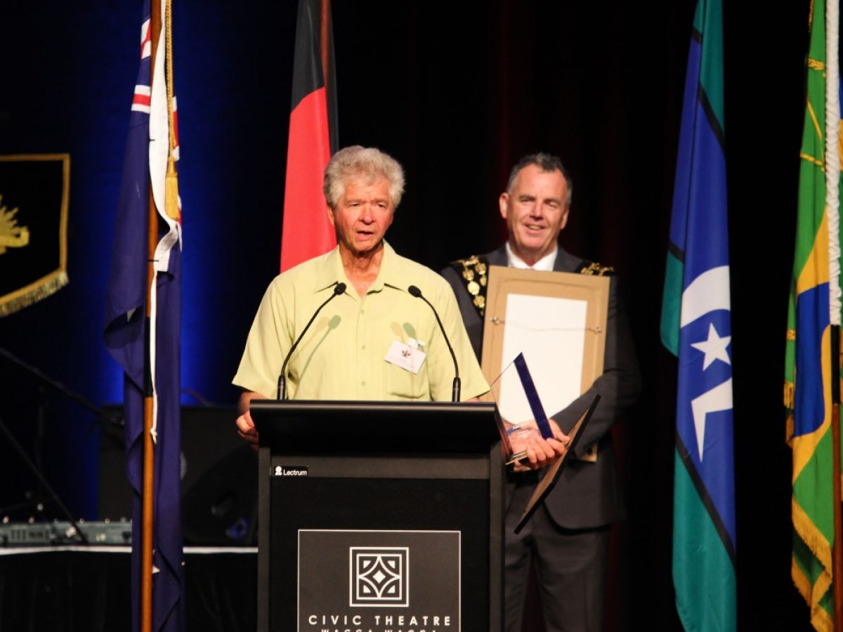 A man speaks at a lectern as another man watches on