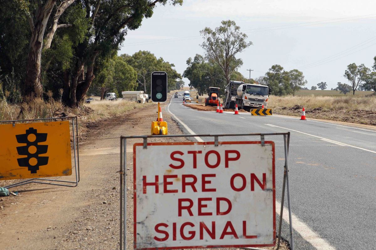 Temporary traffic lights and stop here on red signal sign in foreground with road works in background