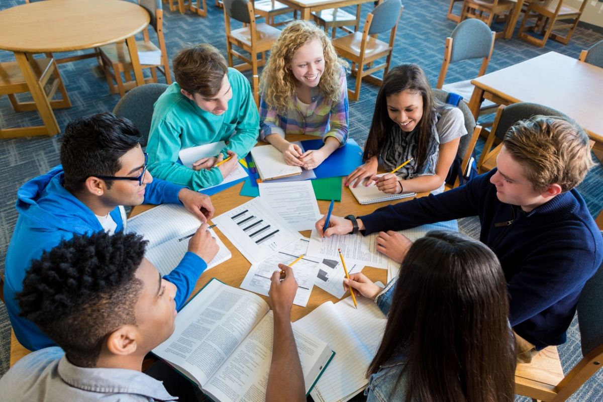 Top view of young people around table with books and laptops