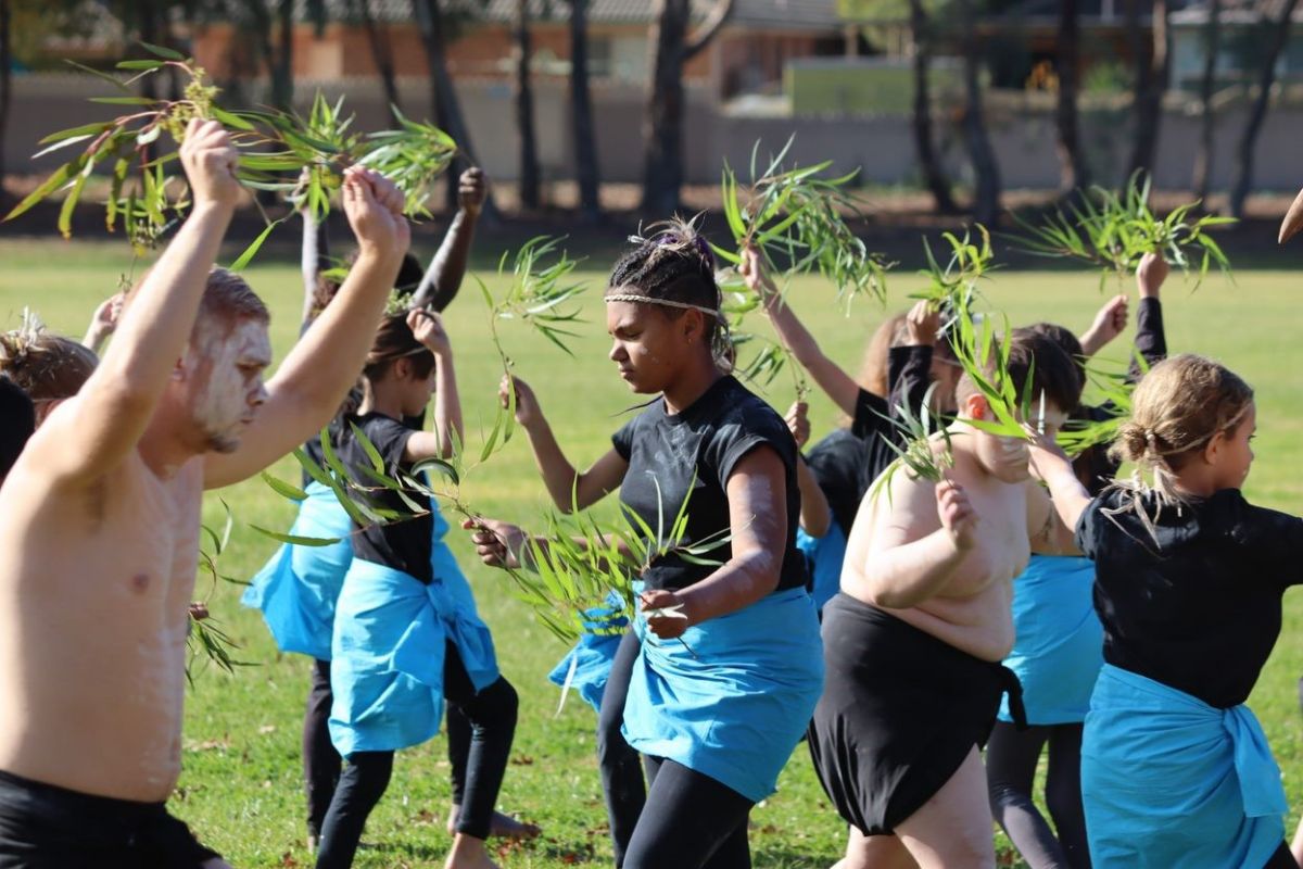 Young First Nations people dancing in a field holding gum leaves.