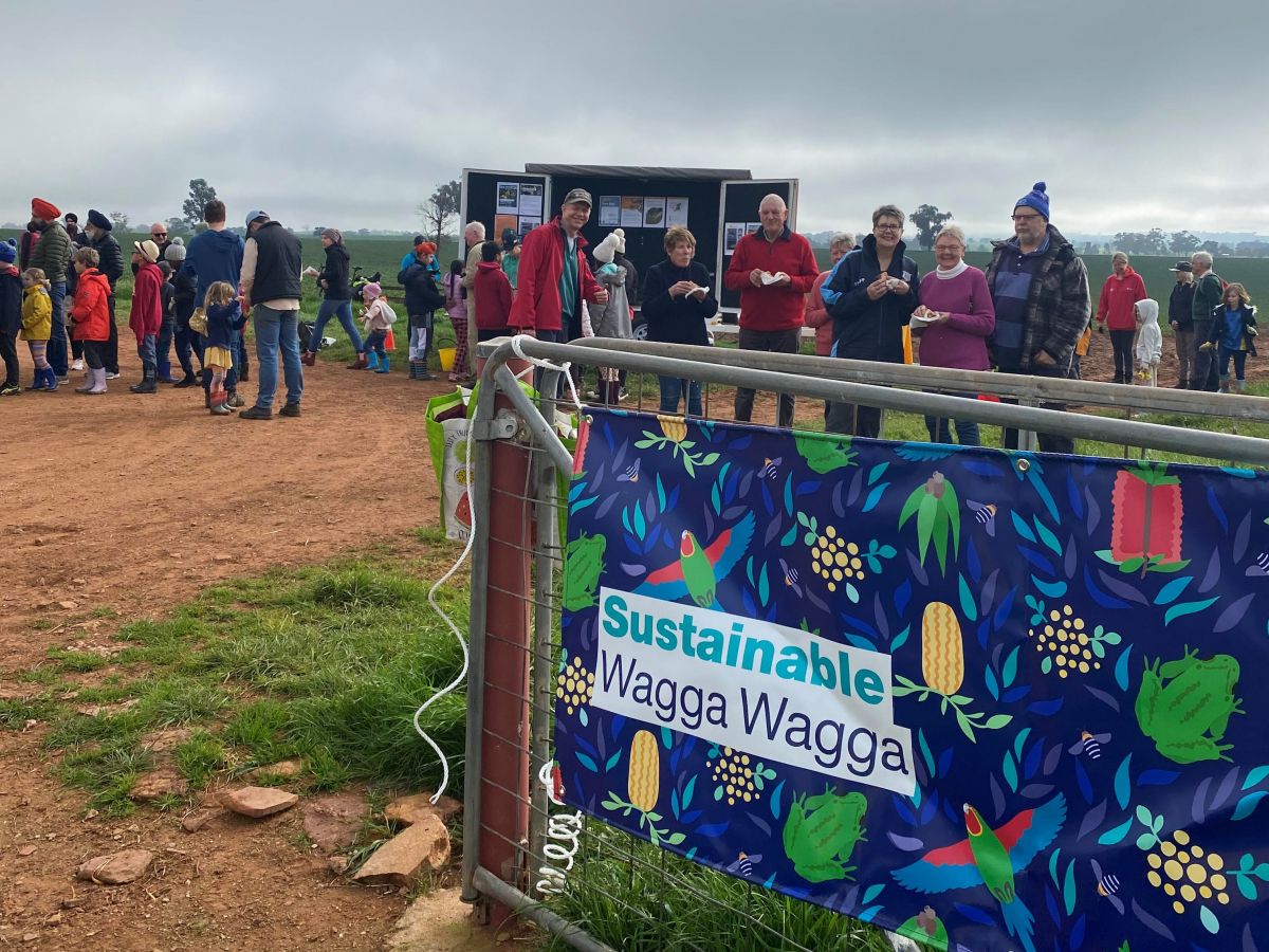 Wide shot of volunteers at standing around after planting finished. Large blue sign on gate with text: 