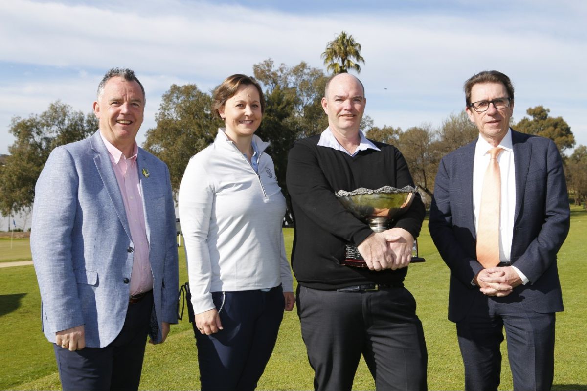 Three men and woman standing on Wagga Wagga Country Club golf course, with trees and lake in background