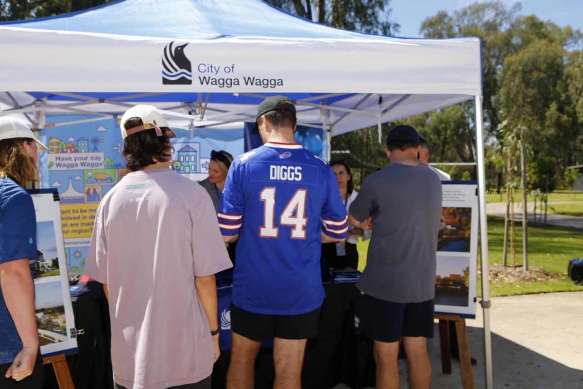 A group of young men speak to two female Council employees at a pop up information marquee about to project proposals for Wagga Wagga