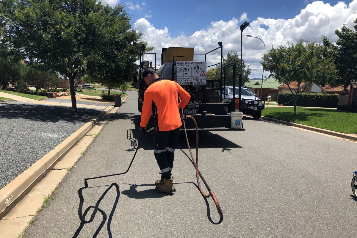 A man sprays a sealant on a road surface filling in cracks. 