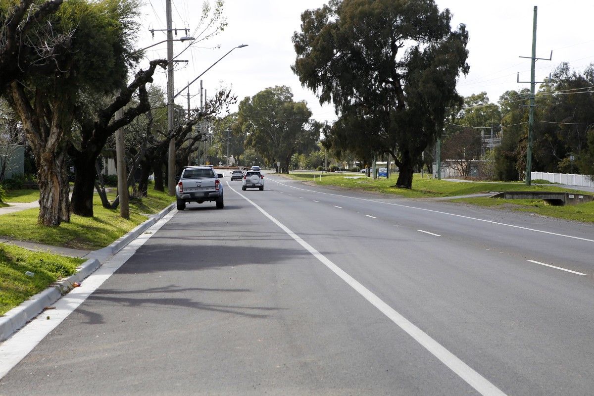 Upgraded asphalt road with line markings and vehicles in the background.