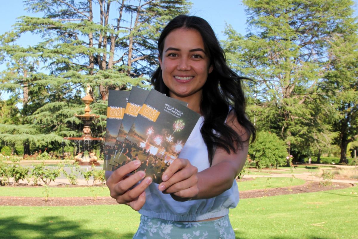 A woman stands outside and is holding a handful of Council's latest Summer What's On guides. 