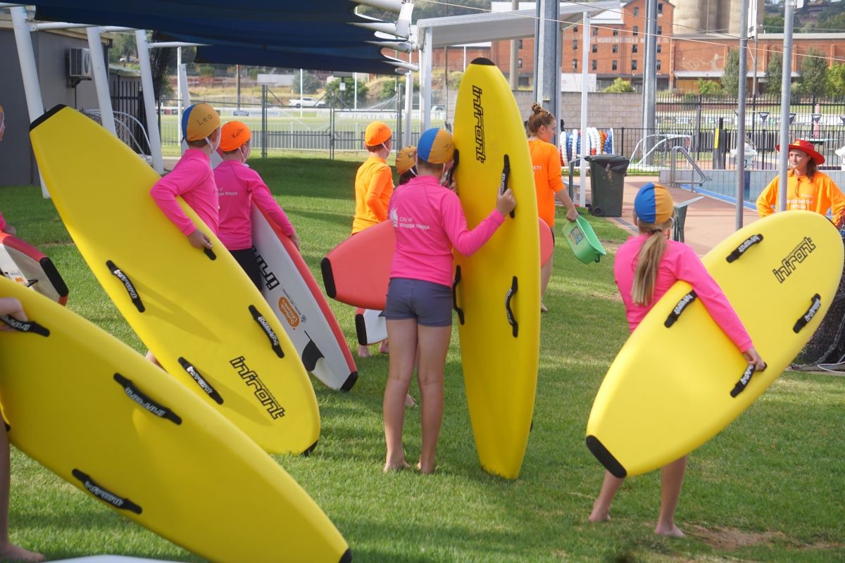 Students at 2025 Outback Lifesavers about to enter the Oasis outdoor pool with boards.