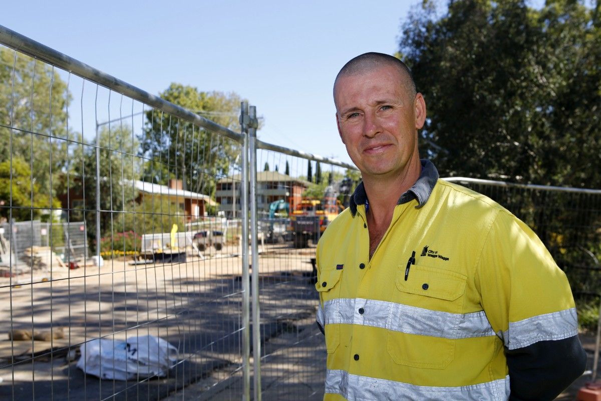 Man in hi-vis shirt looking at camera, with construction site and machinery on bridge in the background.