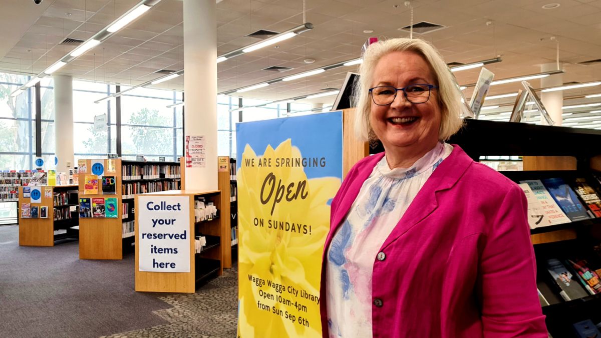 woman next to poster in library with shelves of books nearby