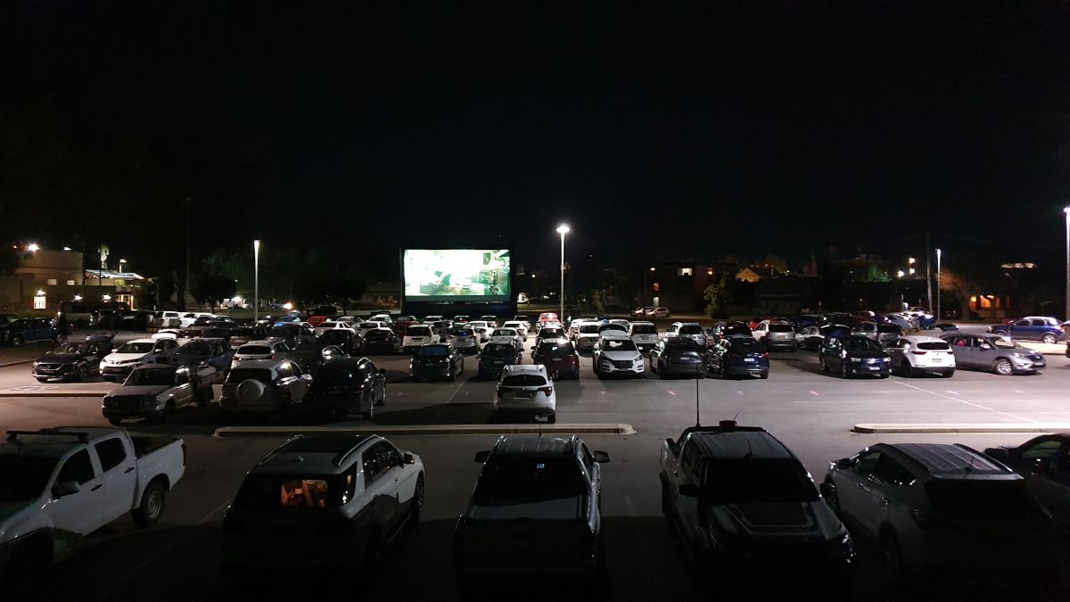 vehicle in carpark at night time, pop up cinema screen with film playing