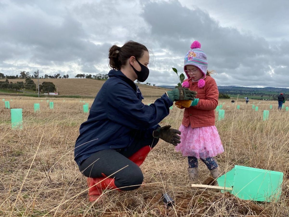 A young girl holding a seedling as her mother looks on