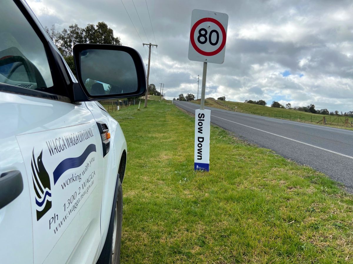 Vehicle next to speed sign with 'Slow Down' sign on it