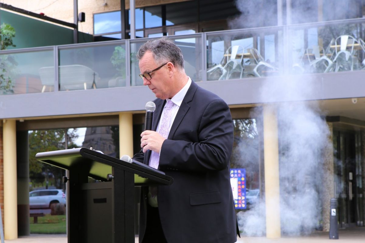 Man standing at podium with smoke rising in background