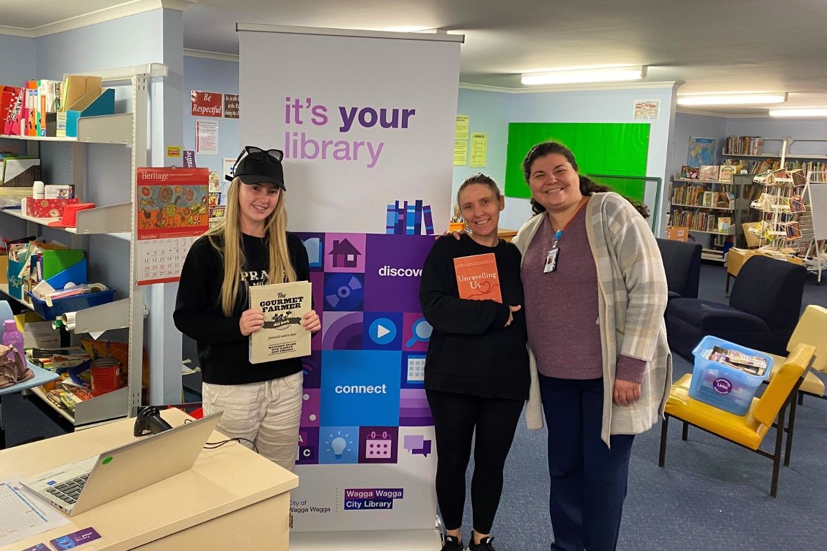 Three women standing next to Your Library banner