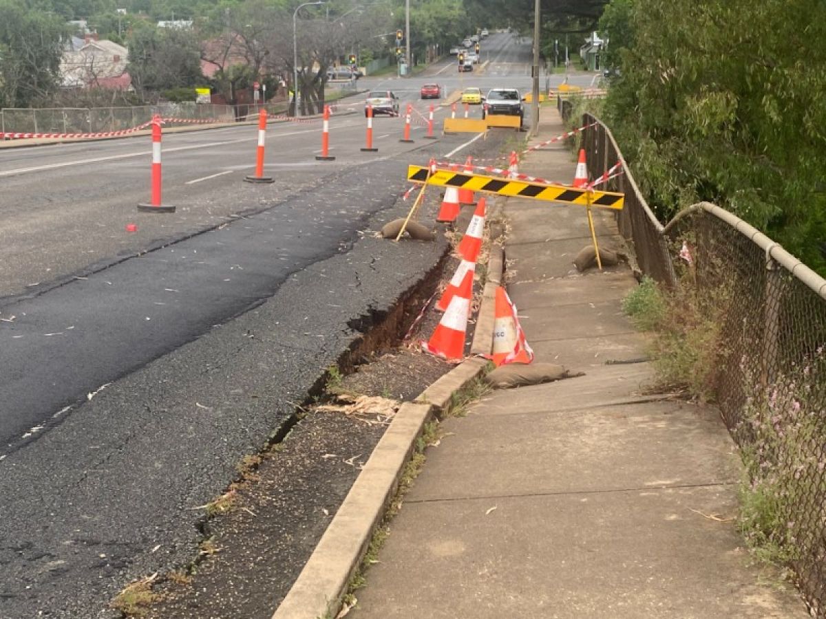 A section of deeply sunken footpath marked off by traffic cones and tape