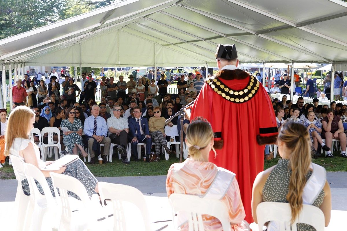 Man in rob at podium in front of crowd under marquee