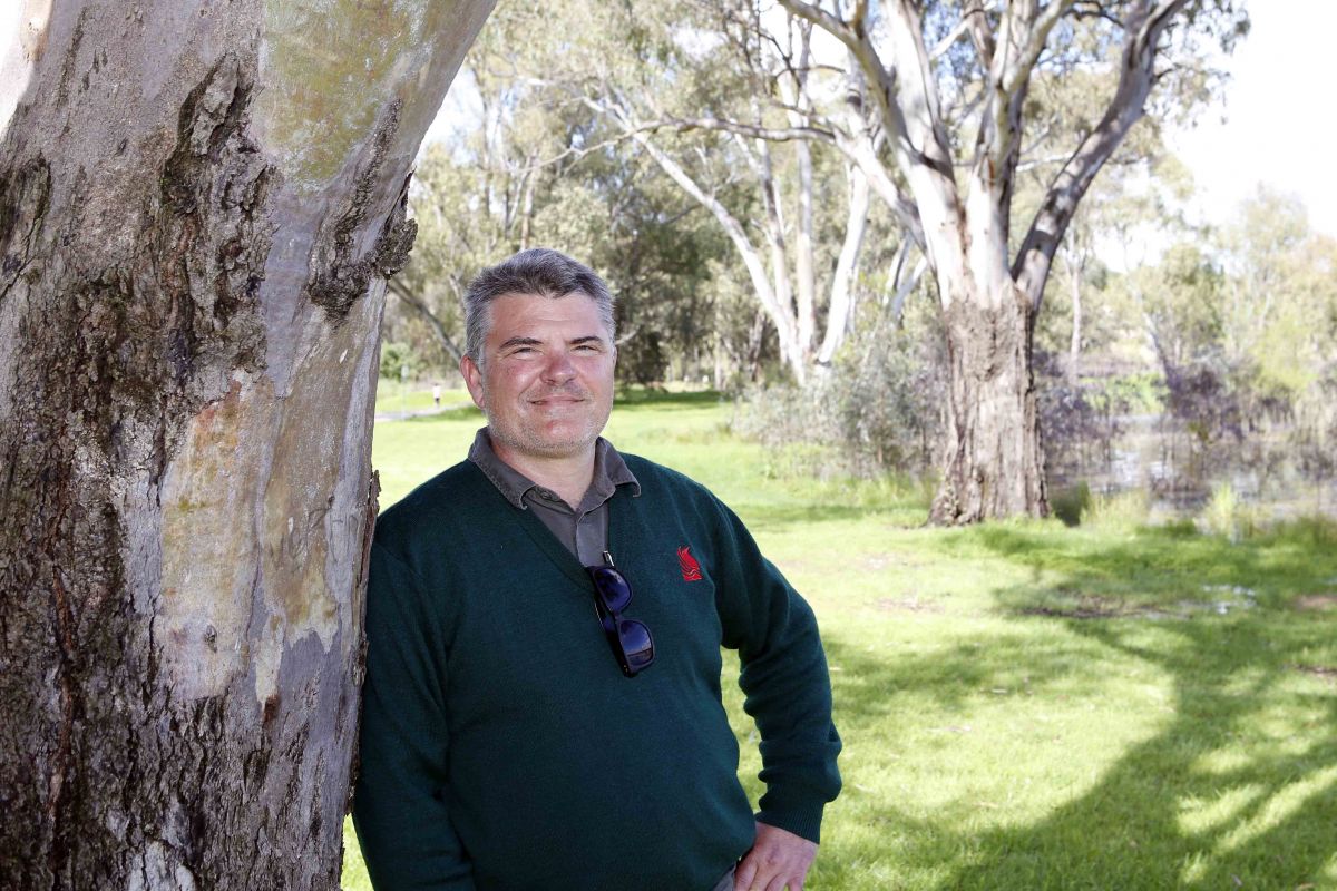 Man in council jumper leaning again tree trunk