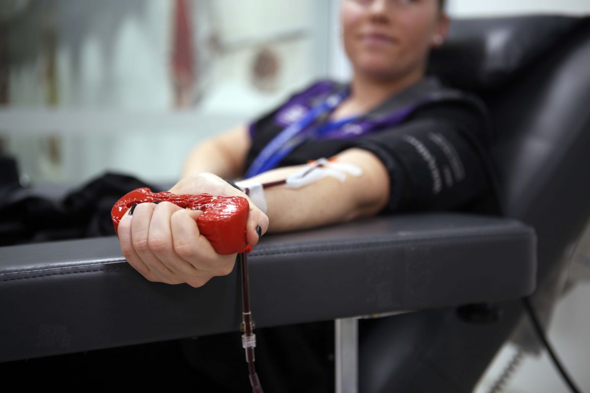 Woman sitting in chair donating blood, with focus on her hand squeezing a stress ball 