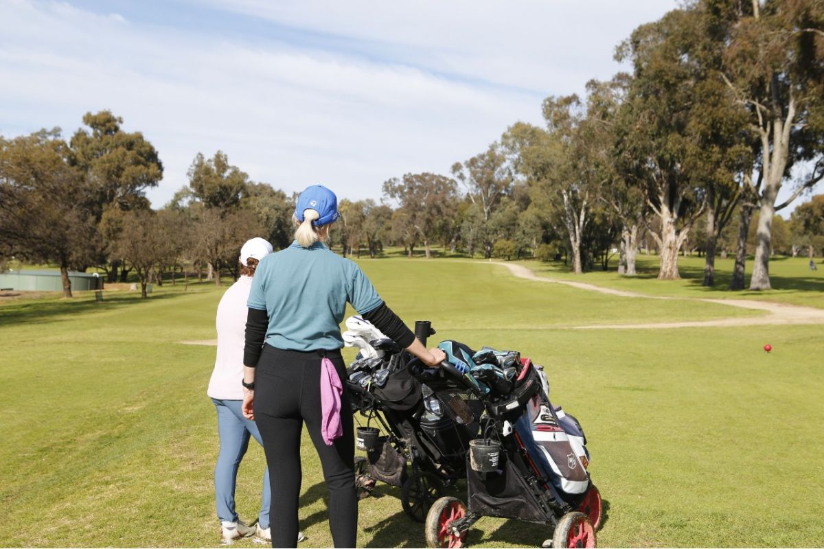 Back view of two women about to head out on golf course, with fairway in the background