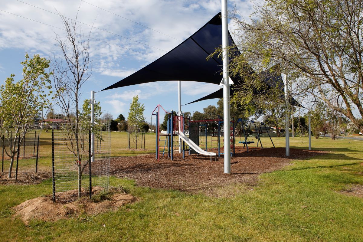 A children's playground with trees around it, and navy blue shade sails. 
