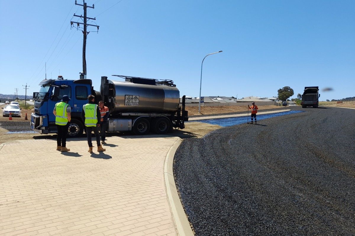 Four men in hi-vis vests near a bitumen truck at roadworks site.