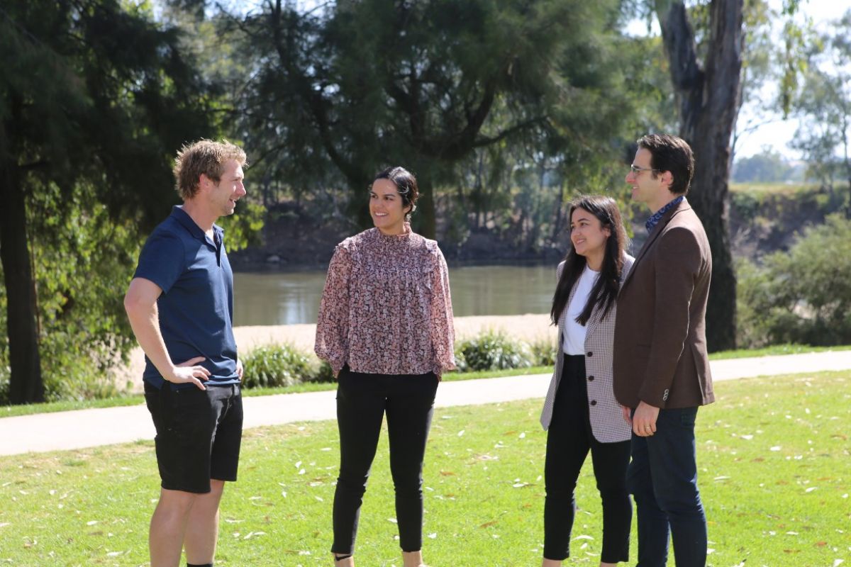 Two men and women standing on grass at the Wagga Beach, with the Murrumbidgee River in background.