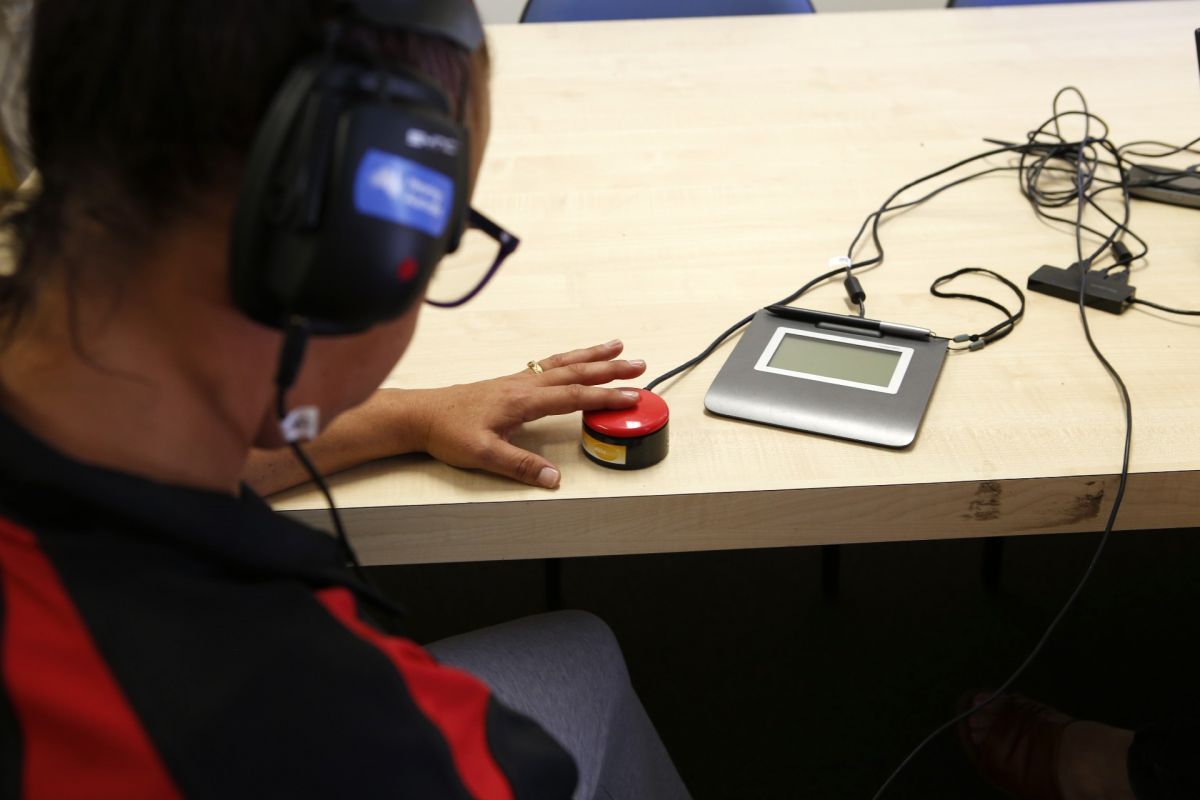 Back view of woman wearing headphones and pressing button on desk as part of hearing test.